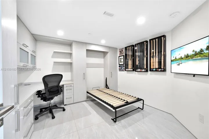 Custom built-in desk with extensive cabinetry, integrated Murphy bed, sleek tile flooring, and wall-mounted display cases