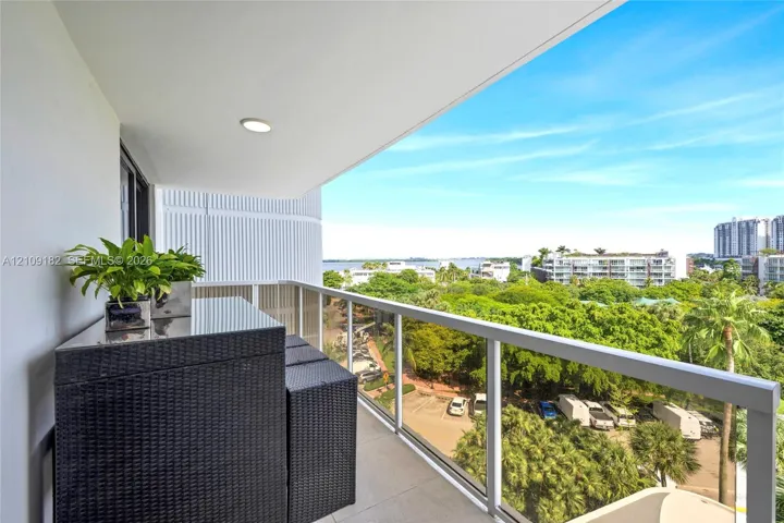 Covered balcony featuring tile flooring and a glass railing with metal framing, overlooking coastal foliage and water