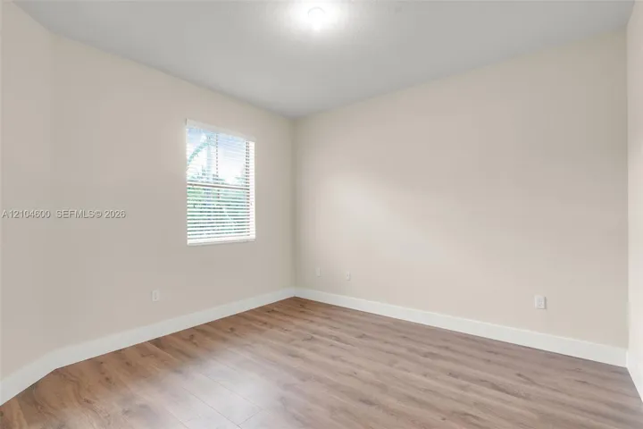 Neutral-toned interior space featuring wood-finish flooring, crisp white trim, and a window with horizontal blinds