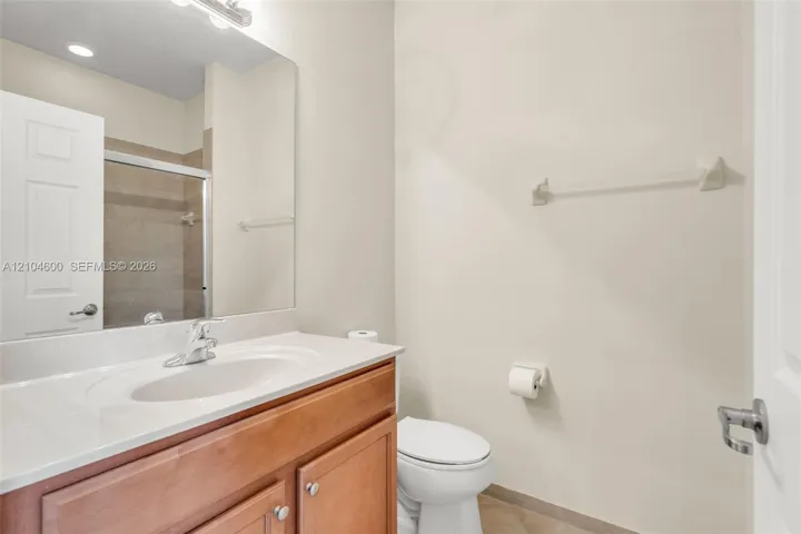 Bathroom vanity with a solid-surface integrated sink, wood-finish cabinetry, a large wall-mounted mirror, and a shower enclosure with a sliding glass door