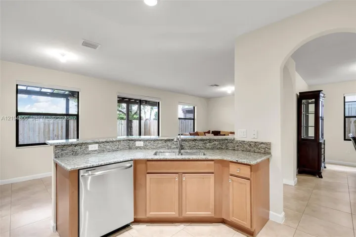 Kitchen featuring stone-finish countertops, stainless steel dishwasher, double-basin sink, wood-finish cabinetry, and ceramic tile flooring