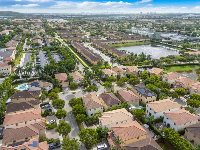 Aerial view of a residential community featuring tile roofs, mature palm trees, landscaped green spaces, and a central water feature
