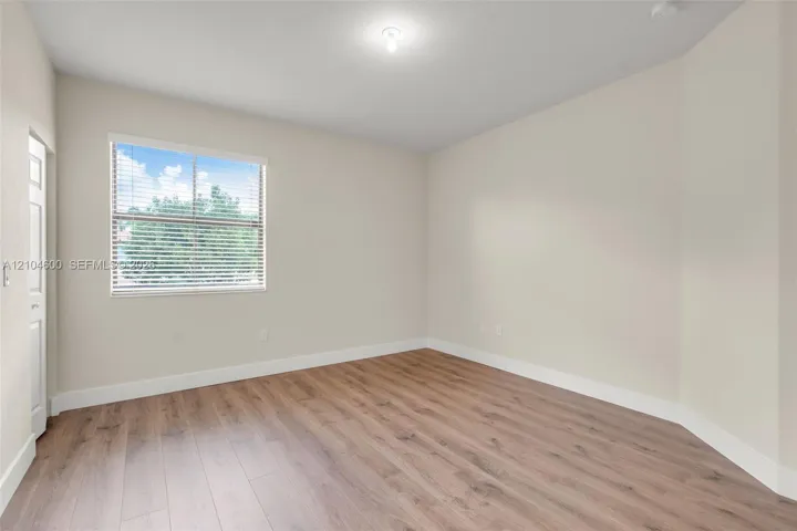 Neutral interior space featuring wood-finish flooring, light-toned walls, and a window with horizontal blinds