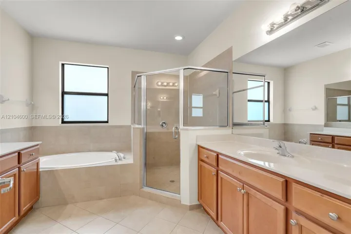 Bathroom featuring a soaking tub, separate glass-enclosed shower with tile surround, wood-finish cabinetry, countertop with integrated sink, and large wall-mounted mirror