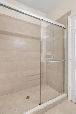 Walk-in shower featuring a sliding glass door with brushed metal hardware, neutral tile surround, integrated shelving, and diagonal tile flooring