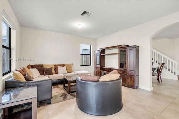 Living area featuring neutral-toned tile flooring, built-in wooden cabinetry, arched architectural opening, and white staircase with matching railing