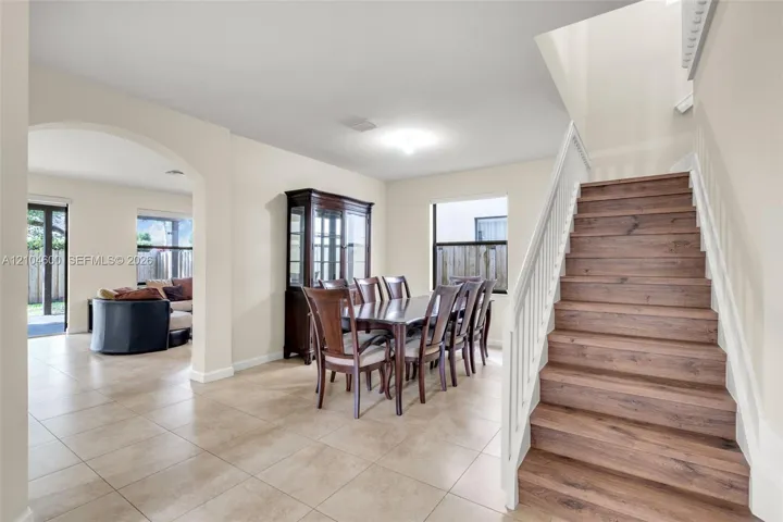 Interior featuring a staircase with wood-finish treads and white balusters, light-colored ceramic tile flooring, and a large arched entryway