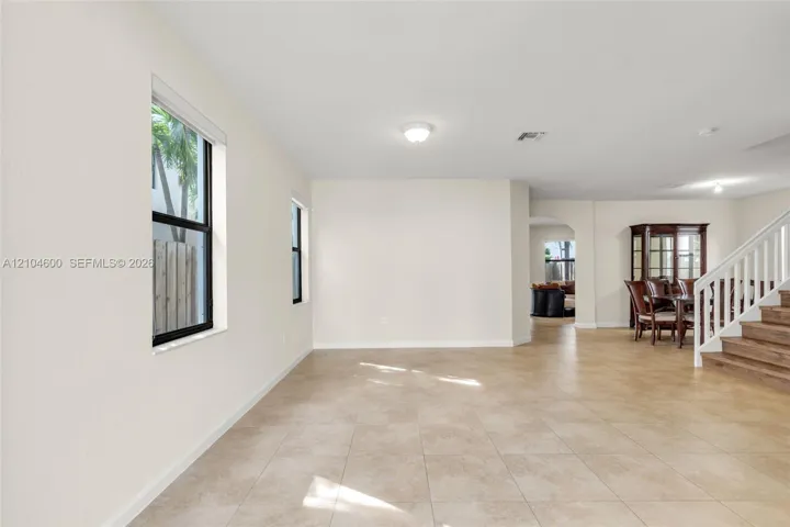 Open-concept area featuring neutral wall tones, large-format tile flooring, oversized windows with black frames, and a wooden staircase with white balusters
