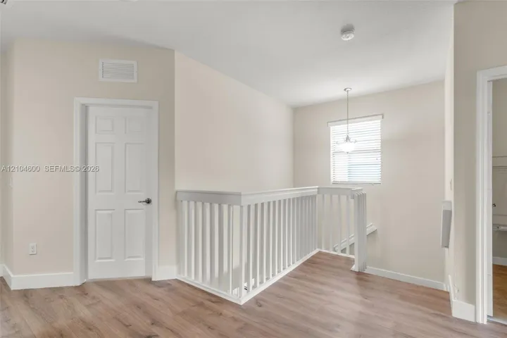 Wood-finish flooring, white railing, neutral wall tones, and overhead pendant lighting