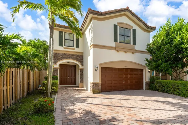 Two-story exterior featuring a stone veneer facade, paver driveway, arched entryway, double front doors, and attached multi-car garage
