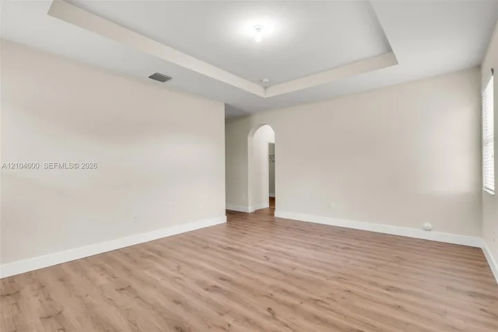 Interior space featuring a recessed tray ceiling, neutral wall tones, wood-finish flooring, and an arched entry