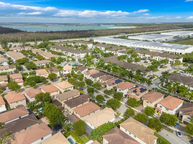 Aerial perspective of a multi-unit residential community featuring clay tile roofs, integrated solar panel arrays, dense mature landscaping, and paved streets