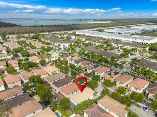 Aerial perspective of a multi-story residence with a pitched tile roof, situated within a landscaped suburban community featuring mature trees and paved street access