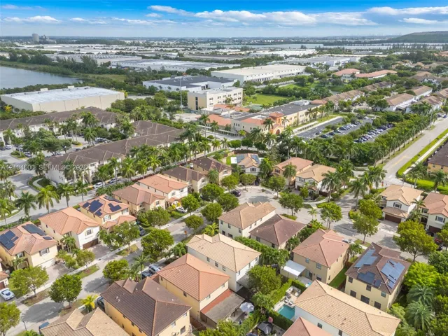 Aerial perspective of a planned community featuring multi-level residential structures, tiled roofing, solar panel installations, and established tropical landscaping