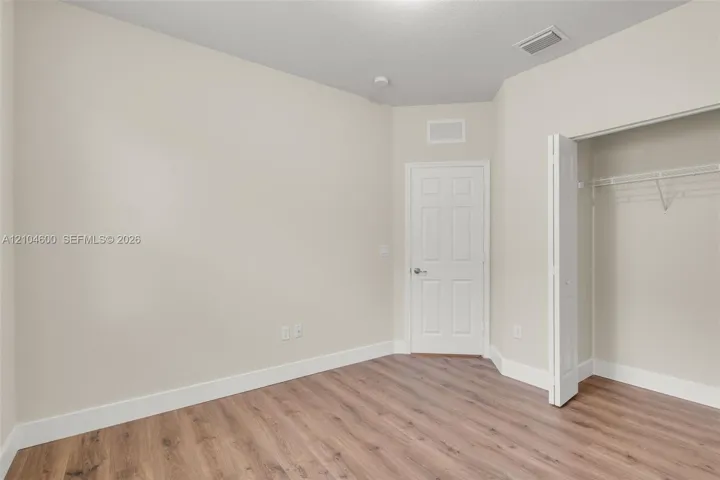 Interior room featuring neutral-toned walls, wood-finish flooring, a solid-core interior door, and a walk-in closet with built-in wire shelving