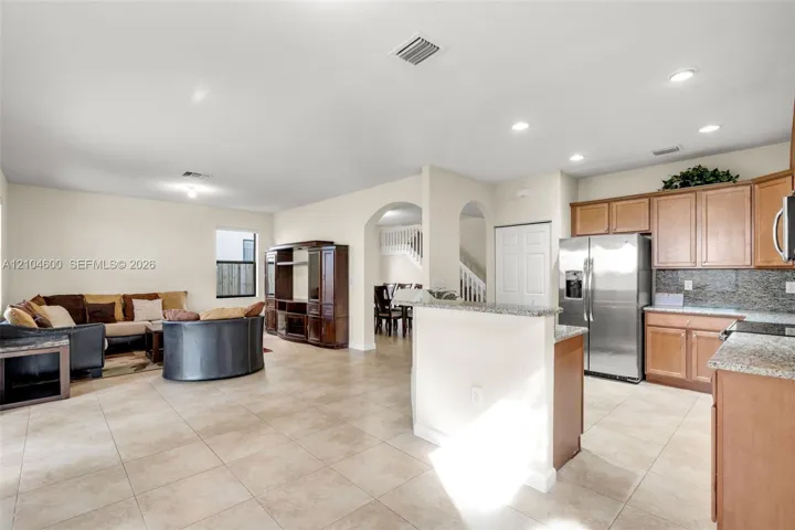 Kitchen featuring wood cabinetry, stone countertops, and stainless steel refrigerator, complemented by tile flooring and arched architectural doorways