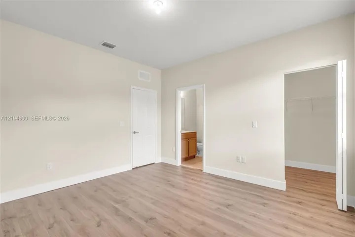 Interior space featuring wood-finish flooring, neutral wall tones, a six-panel door, and a walk-in closet with built-in shelving