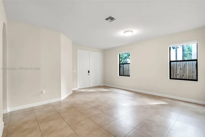 Neutral-toned interior space featuring light-colored tile flooring, double entry doors, and dual windows with black frames