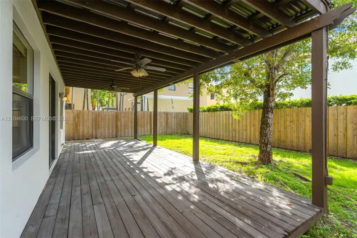 Covered wood patio featuring an overhead pergola, dual built-in ceiling fans, a wooden privacy fence, and a green lawn
