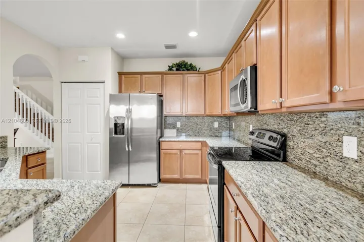Kitchen featuring light wood cabinetry, stone countertops, coordinating stone backsplash, stainless steel refrigerator, and built-in microwave