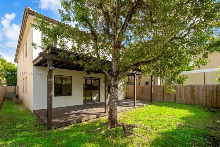 Stucco exterior featuring a wood pergola, attached deck, fenced perimeter, and mature tree