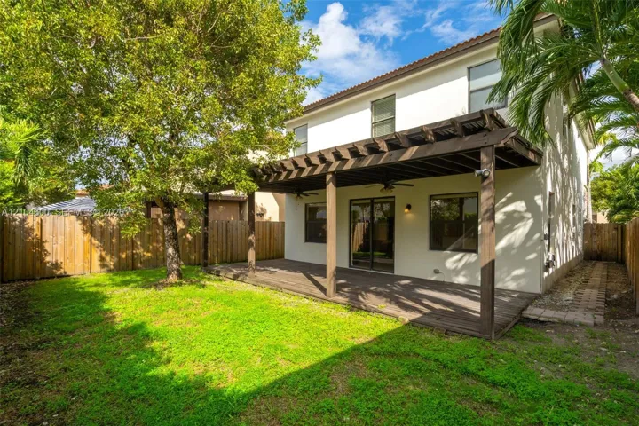 Stucco exterior featuring a wood-tone pergola, integrated ceiling fans, a wood-finish deck, and a fenced backyard