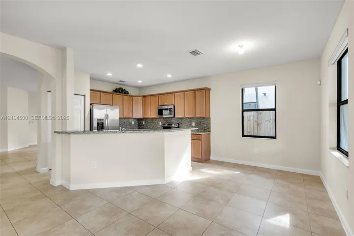 Kitchen featuring wood cabinetry, stone-finish countertops, stainless steel appliances, tile flooring, and recessed lighting