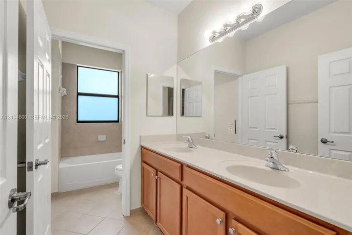 Dual-vanity cabinetry with an expansive solid-surface countertop, full-width wall mirror, chrome-finish fixtures, and a tiled tub-and-shower combination