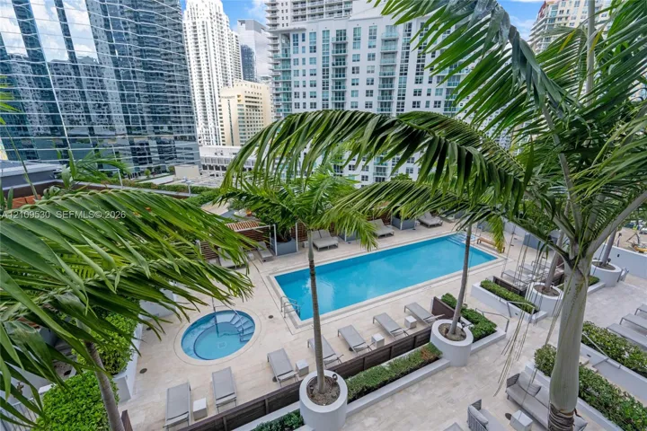 Outdoor terrace featuring a rectangular swimming pool, circular spa, natural stone decking, and mature palm trees