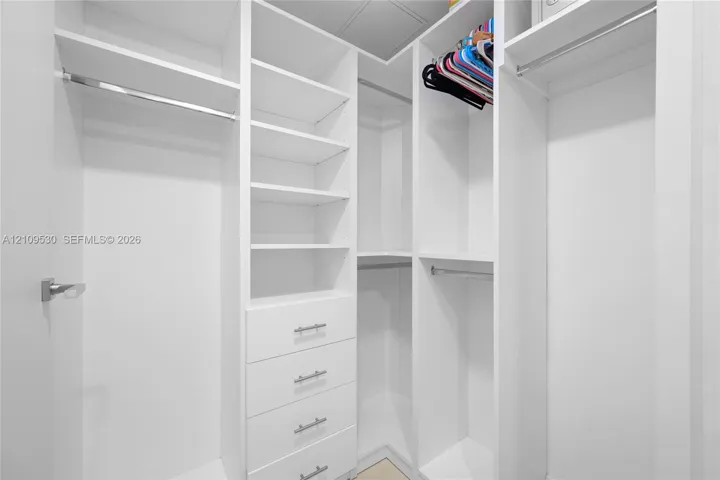 Custom walk-in closet featuring white built-in shelving, four integrated storage drawers with brushed metal pulls, and multiple tiered hanging rods