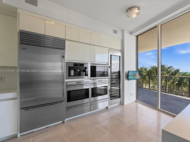Kitchen featuring high-gloss cabinetry, stainless steel professional-grade appliances, built-in coffee station, integrated wine refrigeration, and floor-to-ceiling glass paneling