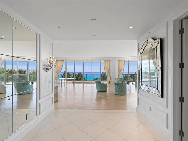 Entryway featuring large-format tile flooring, floor-to-ceiling mirrored wall panels, decorative wall molding, and recessed lighting, leading into a spacious room with herringbone wood-finish flooring and floor-to-ceiling glass panel windows