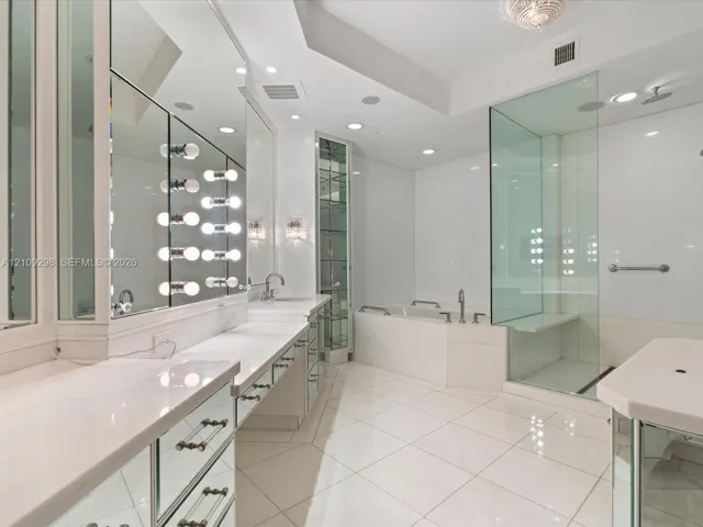 Bathroom featuring expansive vanity with mirrored cabinetry, built-in glass shelving, deep soaking tub, and a frameless glass-enclosed shower with built-in bench