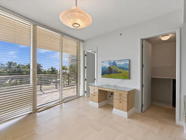 Floor-to-ceiling windows with integrated horizontal blinds, parquet-patterned wood-finish flooring, custom built-in light-wood desk with glass top, and textured semi-flush mount ceiling lighting
