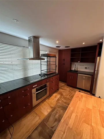 Kitchen featuring rich wood cabinetry, stainless steel appliances, dark countertops, and varied stone tile flooring