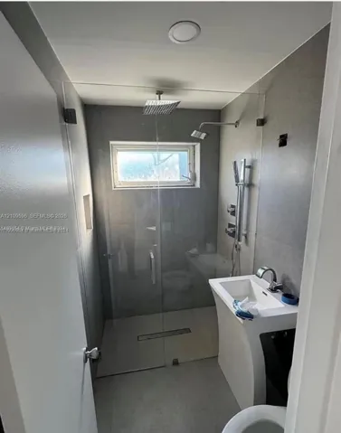 Walk-in shower with a glass enclosure, square rainfall showerhead, handheld shower fixture, recessed wall niche, and pedestal sink with a chrome faucet