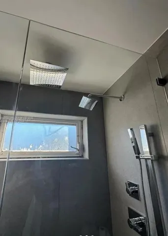 Walk-in shower featuring large-format tile surround, rainfall showerhead, adjustable handheld shower fixture, glass enclosure, and window