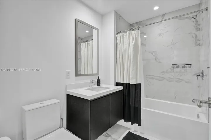 Floating vanity with a white countertop and rectangular basin, full-height wall tiling in the shower area, and recessed ceiling lighting