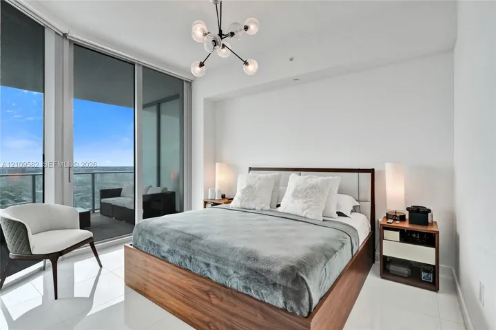 Floor-to-ceiling glass sliding doors, private balcony with metal railing, polished tile flooring, and multi-arm geometric ceiling light fixture