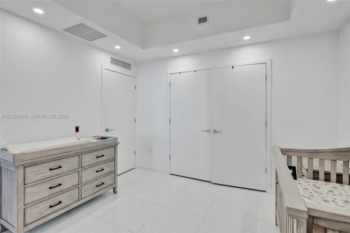 Interior room featuring white tile flooring, recessed ceiling lighting, a tray ceiling, and double-door closet cabinetry