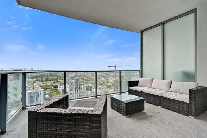 Covered private balcony featuring concrete flooring, floor-to-ceiling glass paneling, and a metal railing