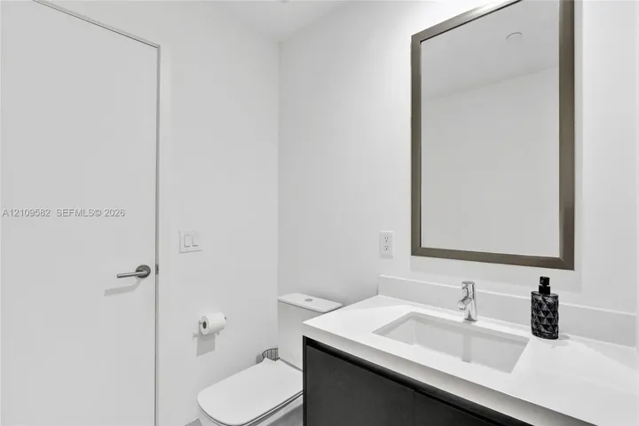 Modern vanity with a light-toned countertop, rectangular undermount sink, chrome faucet, and dark-finish base cabinetry, accompanied by a framed mirror