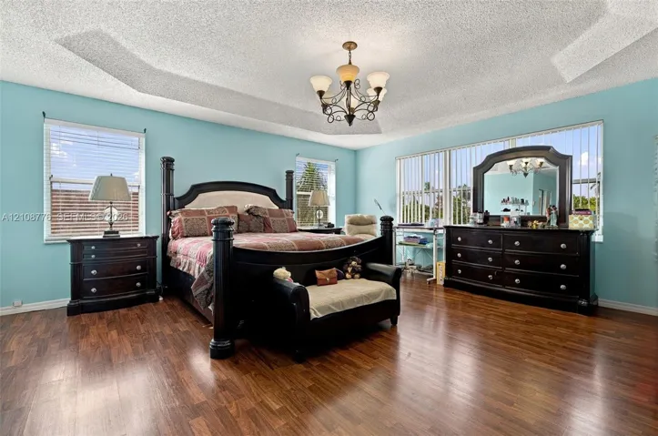 Tray ceiling with central chandelier, wood-finish flooring, and expansive windows with vertical blinds
