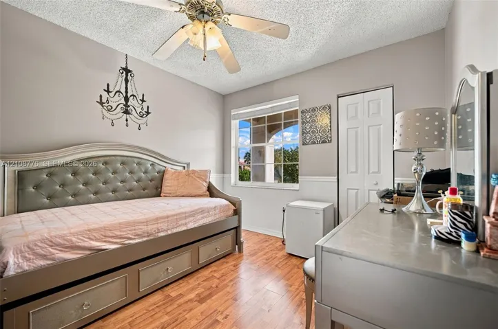 Wood-finish flooring, multi-pane window with grid pattern, decorative hanging chandelier, ceiling fan with integrated lighting, and white bi-fold closet doors