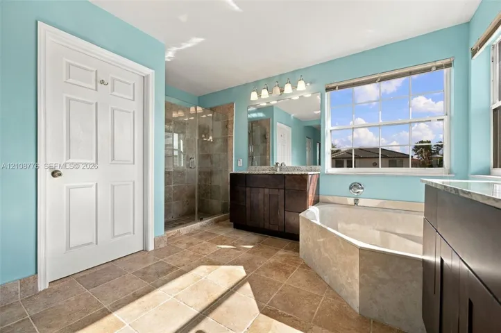 Bathroom featuring dark wood-finish cabinetry, a stone-surround soaking tub, a tiled walk-in shower with a glass enclosure, and natural stone flooring