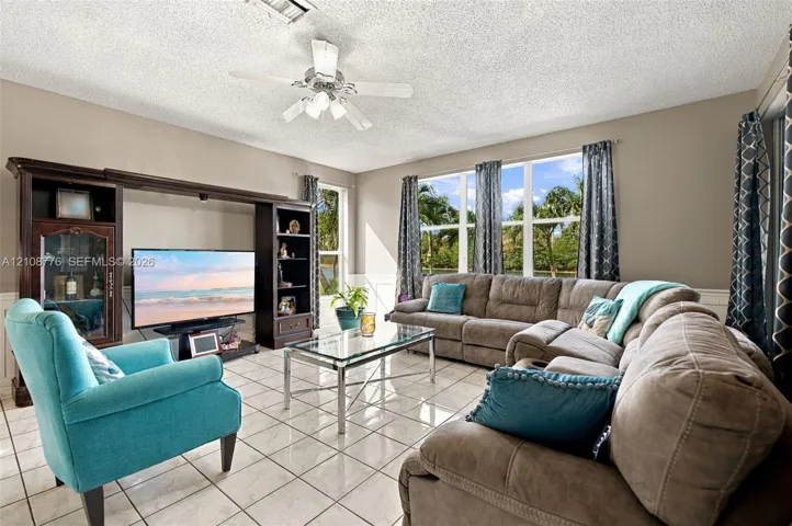 Living area featuring large format tile flooring, built-in wall cabinetry, multi-pane windows, and a ceiling fan