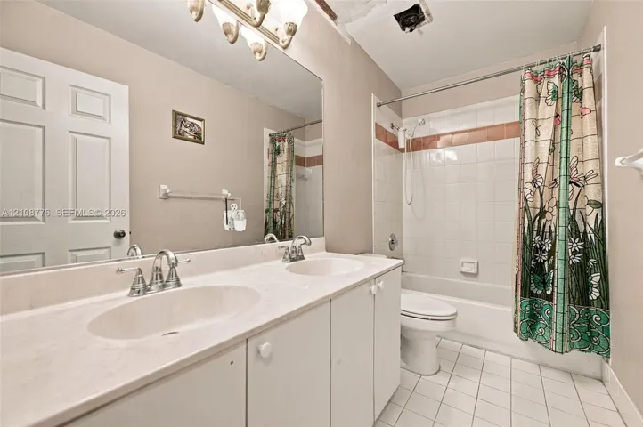 Double vanity featuring integrated oval basins, expansive wall-to-wall mirror, white cabinetry, tile-surround shower and tub combination, and ceramic tile flooring
