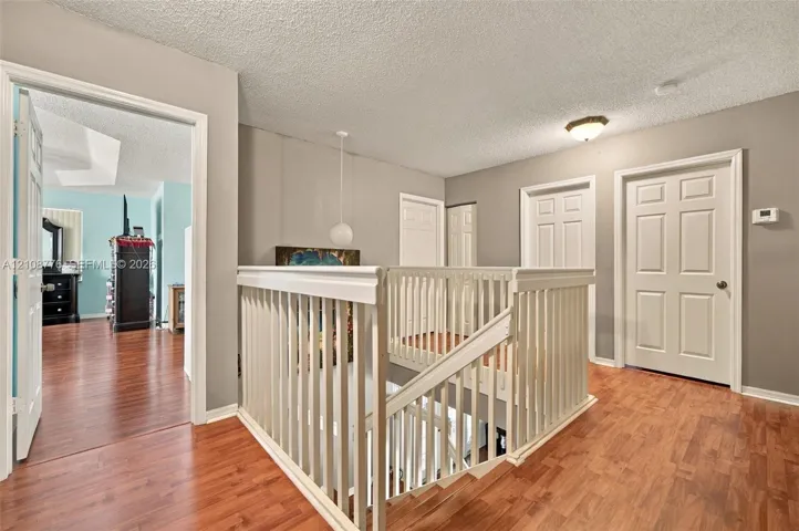Landing featuring wood-finish flooring, white spindle railings, multi-panel interior doors, and a ceiling-mounted light fixture