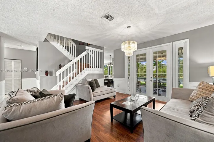 Wood-finish flooring, staircase with white railing, glass-paned French doors, tiered crystal chandelier, and wainscoting