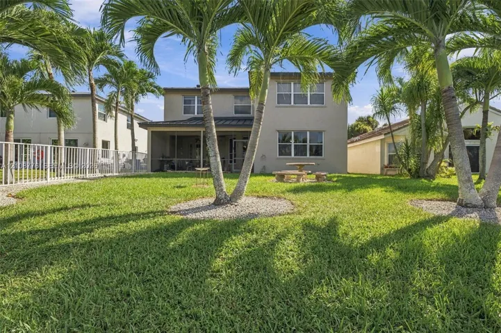 Backyard space featuring a screened-in lanai, mature palm trees, white metal perimeter fencing, and a grass lawn